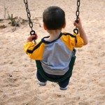 Backside of toddler boy on a swing at the park.