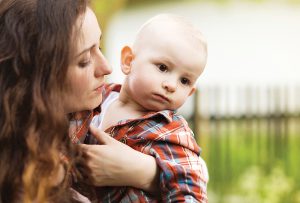 Portrait of a crying little boy who is being held by her mother, outdoors